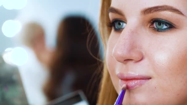 Close up jovem mulher com olhos azuis e cabelos vermelhos colocando brilho labial com escova de maquiagem — Vídeo de Stock