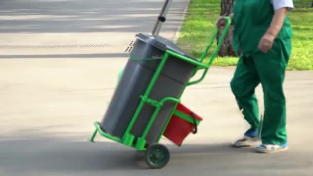 Trabalhador sênior do jardim feminino em lixeira rolante uniforme sobre rodas no parque da cidade — Vídeo de Stock