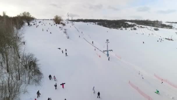 Aérea de esquiadores y snowboarders deslizándose por la ladera nevada y subiendo con telesilla — Vídeo de stock