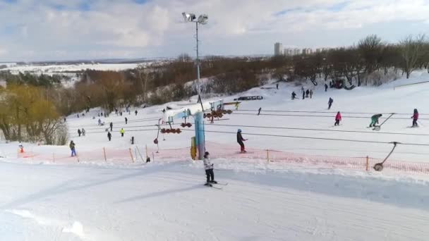 Αεροφωτογραφία του σκιέρ και snowboarders συρόμενη κάτω χιονισμένη πλαγιά και ιππασία με τελεφερίκ — Αρχείο Βίντεο