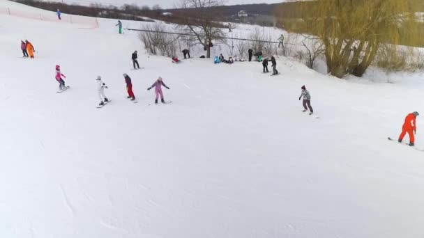 Antenne der Skifahrer und Snowboarder rutscht den verschneiten Hang hinunter und fährt mit dem Skilift hinauf — Stockvideo