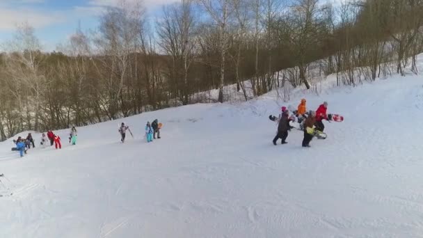 Aérea de snowboarders y esquiadores con equipo en las manos caminando por la ladera nevada — Vídeos de Stock
