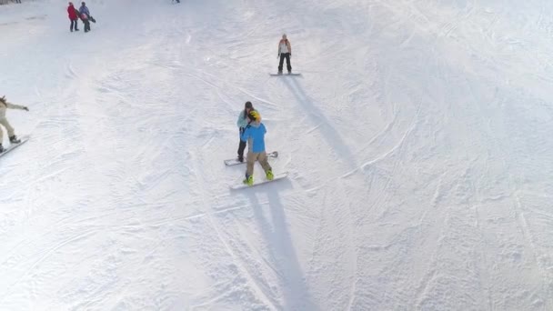 Luchtfoto van professioneel snowboarder helpen van amateur tot snowboard op de besneeuwde helling — Stockvideo