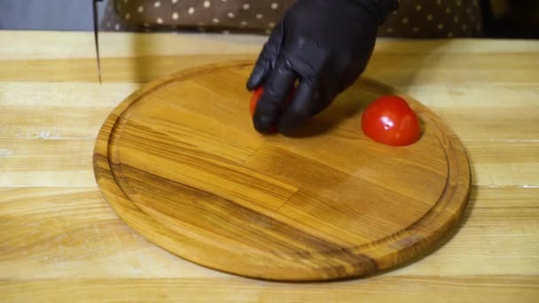 Vista de cerca de las manos del chef en guantes cortando tomate en rodajas en una tabla de cortar de madera redonda — Vídeos de Stock