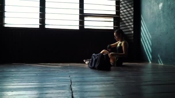 Slowmotion panning ajuste mujer joven con bolsa de deporte sentado en el suelo y envolver la mano con vendaje — Vídeos de Stock