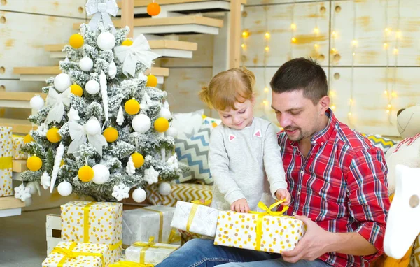 Baba ve yürümeye başlayan çocuk kızı hediyeler Noel ağacı yakınındaki açma