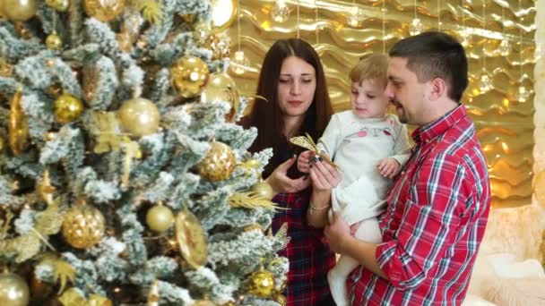 Ευτυχισμένη οικογένεια με παιδί κόρη βάζοντας στολίδι στο χριστουγεννιάτικο δέντρο στο σπίτι — Αρχείο Βίντεο