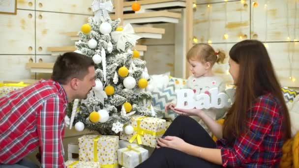 Liten flicka spelar med trä ordet baby nära föräldrar hemma vid jul — Stockvideo