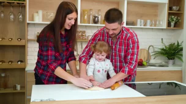 Padres jóvenes y su hijita se divierten juntos rodando masa en la cocina — Vídeos de Stock