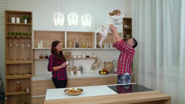 Pai jogando a filha da criança para cima e mãe assistindo-os na cozinha — Vídeo de Stock