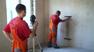 İnşaat işçileri ölçümleri ile site bina üzerinde lazer aracı olun. Erkek işçiler beton duvar üzerinde kırmızı ışın Seviye doğruluğu kontrol. Güvenlik ilkesi, teknoloji, onarım, iç tasarım konsepti