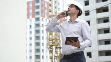 İnşaat sitesi mühendis cep telefonu kontrol üzerinde konuşurken tablet ile inşa teknoloji süreci. Kask içinde erkek mimar iş akışı açık havada denetler. Bina, sanayi, emniyet konsepti
