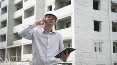 İnşaat sitesi mühendis cep telefonu kontrol üzerinde konuşurken tablet ile inşa teknoloji süreci. Kask içinde erkek mimar iş akışı açık havada denetler. Bina, sanayi, emniyet konsepti
