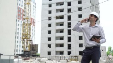 İnşaat sitesi mühendis cep telefonu kontrol üzerinde konuşurken tablet ile inşa teknoloji süreci. Kask içinde erkek mimar iş akışı açık havada denetler. Bina, sanayi, emniyet konsepti