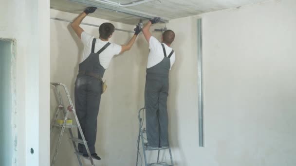 男性ビルダー使用電気ドリル建設敷地に屋内金属製乾式壁プロファイルを組み立てます 安全性 チームワークの概念 — ストック動画