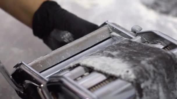 Closeup of hands in gloves rolling black dough in pasta machine in slow motion — Stock Video