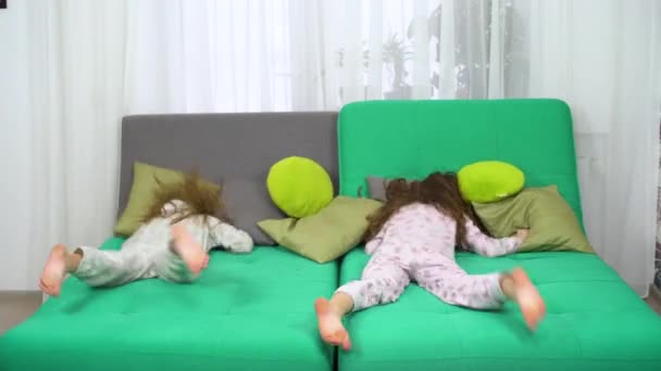 Zwei kleine Mädchen im Pyjama springen auf Sofa ein und beginnen Kissenschlacht — Stockvideo