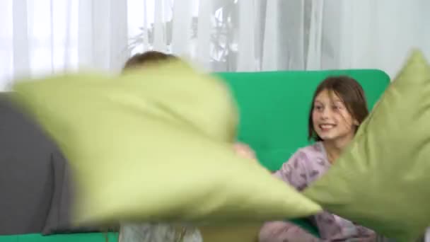 Две маленькие девочки дерутся с подушками на диване — стоковое видео