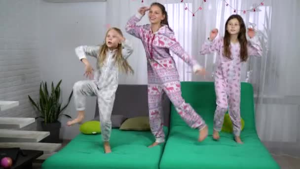 tři roztomilé dívky v pyžamu tanec na pohovce. děti baví spolu doma. přátelství, dětství a volný čas