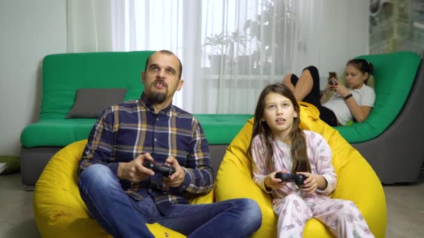 Мужчина и девушка играют с геймпадами дома с другой девушкой на заднем плане — стоковое видео