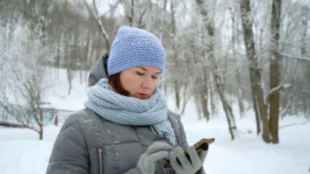 Доросла жінка набирає номер телефону в зимовому парку — стокове відео