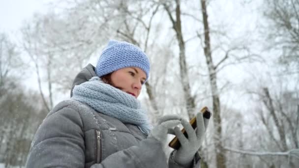 Взрослая женщина читает сообщения по телефону в зимнем парке — стоковое видео