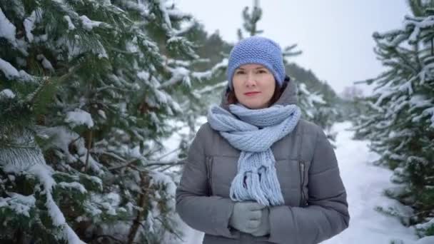 Женщина смотрит в камеру во время прогулки среди сосен в снежном зимнем лесу — стоковое видео