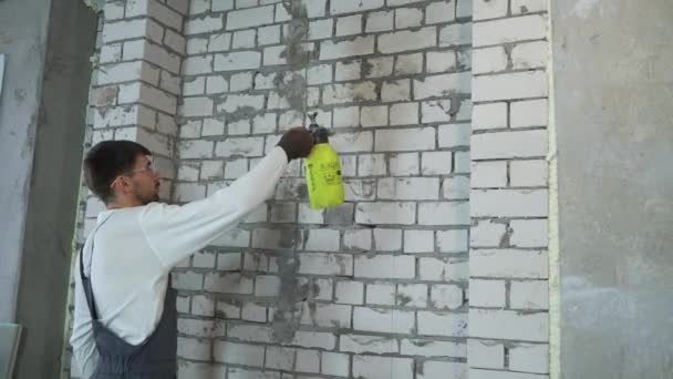 Строитель увлажняет кирпичную стену с помощью распылителя воды — стоковое видео
