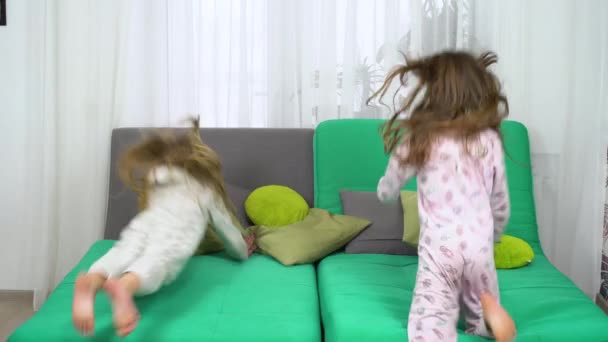 Two little girls fighting with pillows on sofa — Stock Video