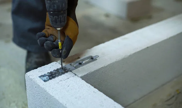Tvůrce šroubování spojovací svorkou v pórobetonu betonového bloku s elektrickou vrtačku — Stock fotografie