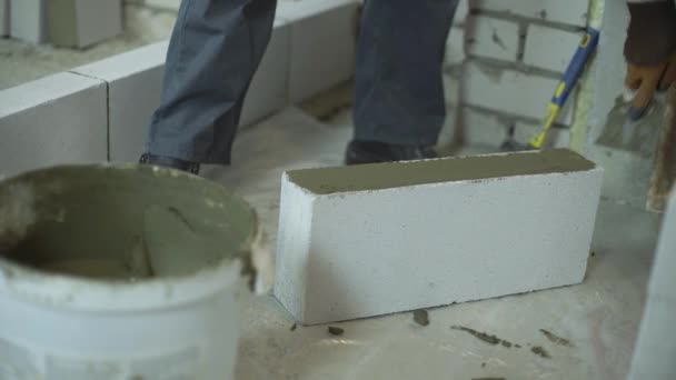Construtor colocando argamassa no lado do bloco de concreto aerado com espátula — Vídeo de Stock