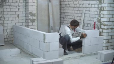 İnşaat işçisi kabarcık seviyesi ile gaz beton duvar düzgünlüğünü kontrol eder. dülger üniforma ve eldiven iç duvar kurmak. ev yenileme, inşaat ve el ile çalışma