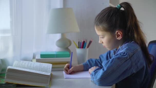 Kleines Schulmädchen macht Hausaufgaben am Tisch — Stockvideo