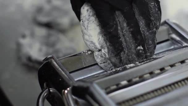 Closeup of hand in glove putting black dough in pasta machine and rolling it — Stock Video