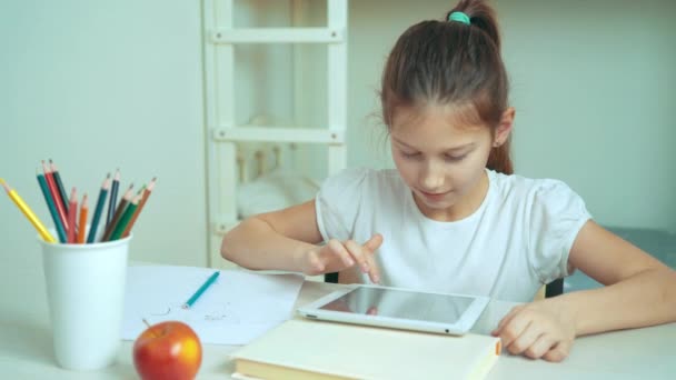 Liten flicka med rött hår spelar spel på tabletten sitter vid bord hemma — Stockvideo