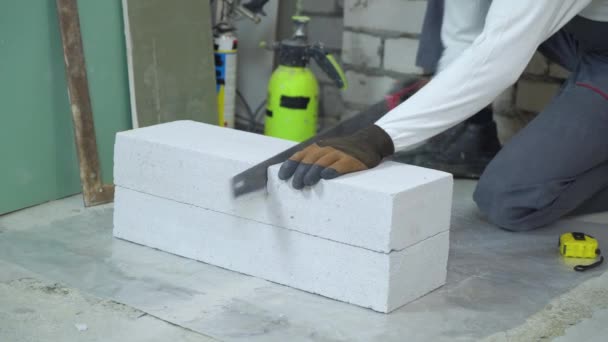 ビルダーの手で気泡コンクリート ブロックを切断を見た 手袋の建設現場でブロックを切断の男性労働者 マニュアル作業 — ストック動画