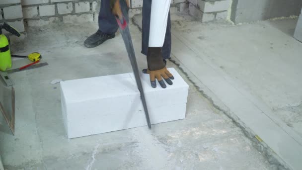 Construtor serrar bloco de concreto aerado ao longo da linha desenhada com serra manual — Vídeo de Stock