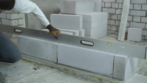 Construction worker checking evenness of aerated concrete wall with bubble level — Stock Video