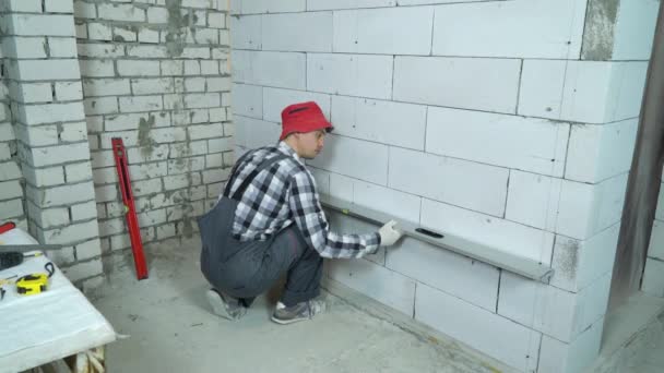 Builder checking quality of aerated concrete block wall with construction ruler — Stock Video
