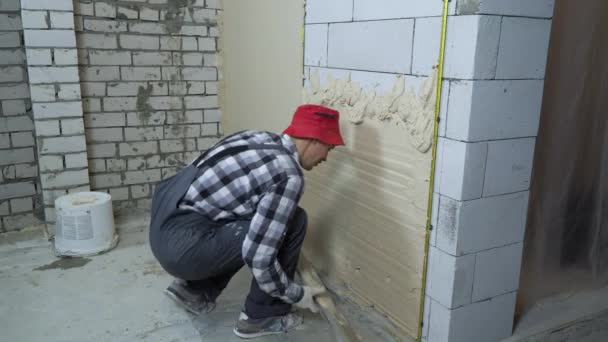 Будівельник розкладає штукатурку на бетонній стіні з будівельним лінійкою — стокове відео