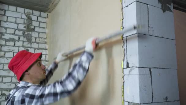 Наклон сглаживающей штукатурки строителя на внутренней стене строительной линейкой — стоковое видео