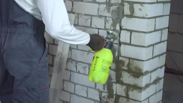 stavební dělník moisturing cihlová zeď s vodou rozprašovačem