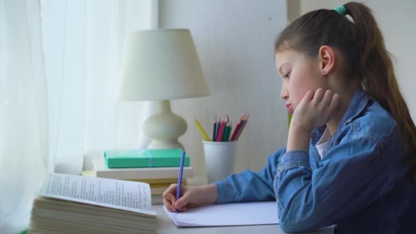 Petite écolière en jean veste faisant des sommes sur feuille de papier à la maison — Video