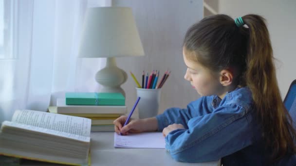 Konzentriertes Schulmädchen in Jeansjacke macht Hausaufgaben auf einem Blatt Papier — Stockvideo