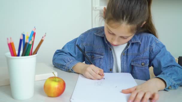 Iskola lány farmert hord, étkezési alma és színes ceruza rajz — Stock videók