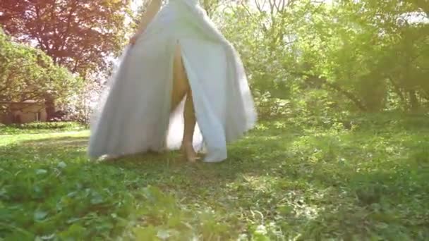 Low shot of woman in long dress walking on green grass in slow motion — Stock Video