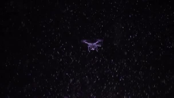 Drone che vola nel cielo notturno con neve che cade e luci flash sullo sfondo — Video Stock
