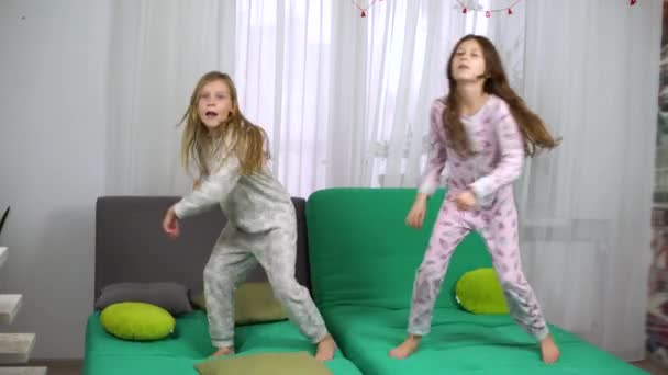 Zwei kleine Mädchen im Pyjama tanzen auf dem Sofa — Stockvideo