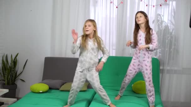 Two little girls in pajamas dancing on sofa — Stock Video