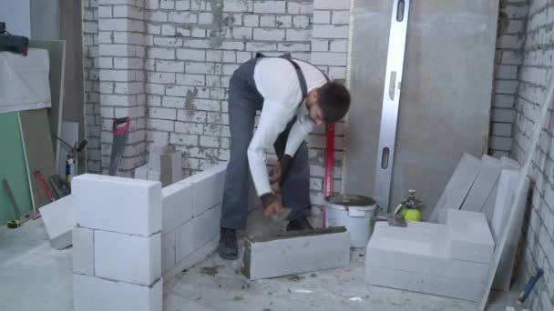 Young caucasian builder putting mortar on sides of aerated concrete block — Stock Video